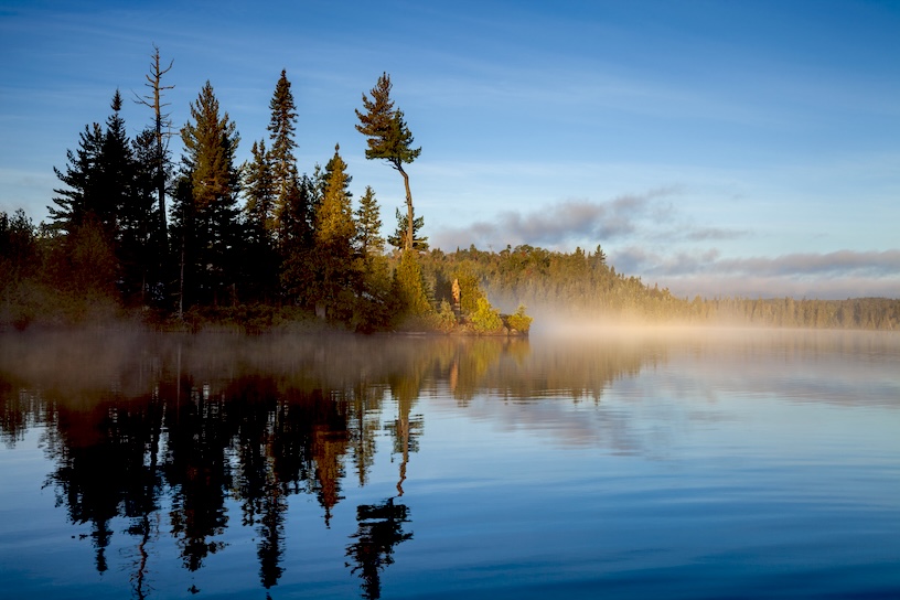 Blue trout lake and island in northern Minnesota with fog on the water at sunrise during September